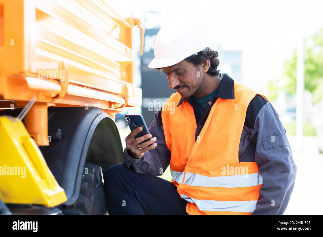 Male engineer standing next to yellow truck looking at smartphone Stock Photo