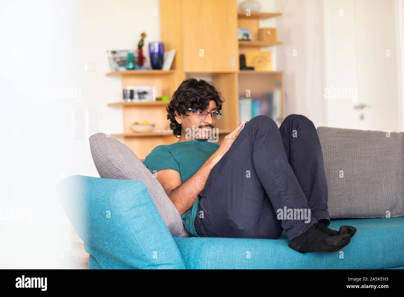 Mid adult man relaxing on sofa looking at smartphone Stock Photo