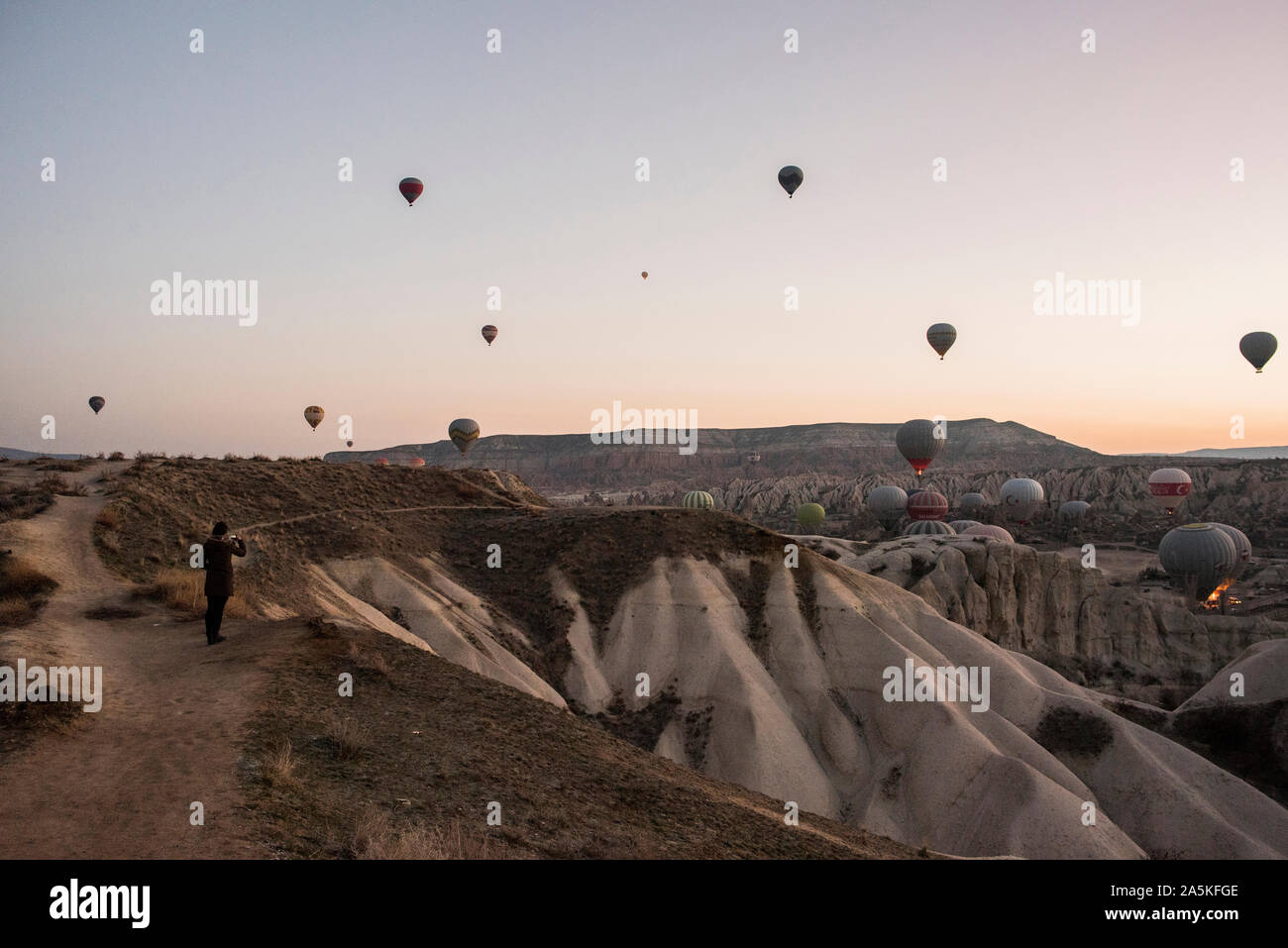 Woman enjoying view and display of hot air balloons in valley, Göreme, Cappadocia, Nevsehir, Turkey Stock Photo