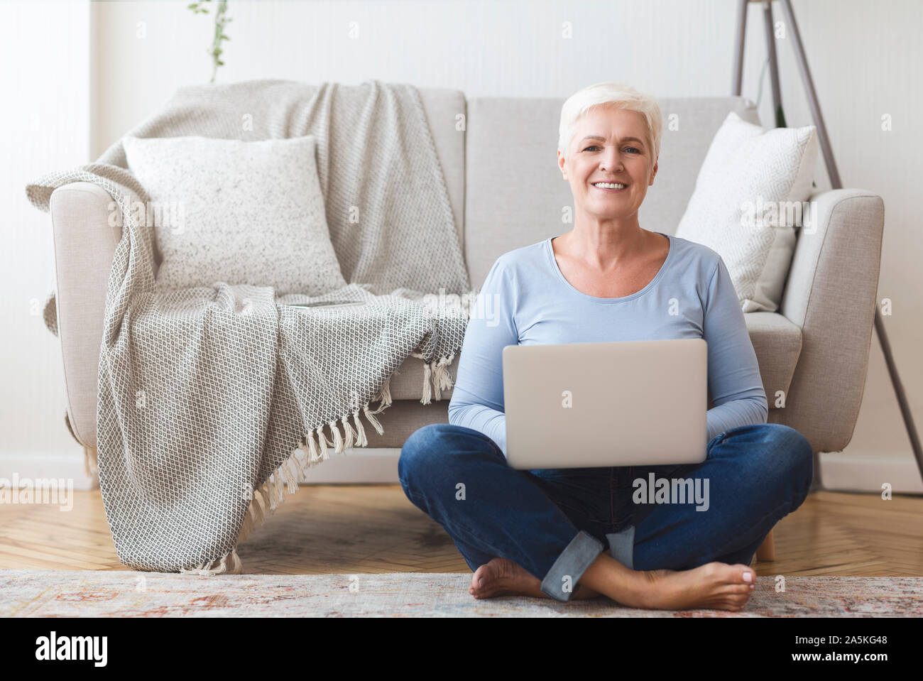 Active old woman sitting on floor and using laptop Stock Photo