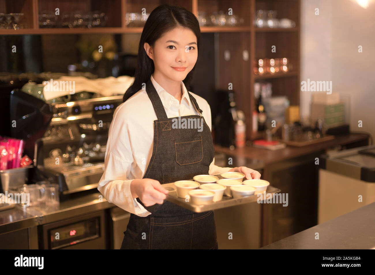 Barmaid standing behind bar counter and holding tray Stock Photo