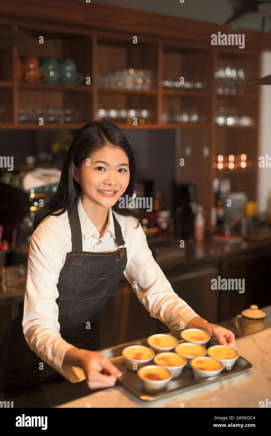 Barmaid standing behind bar counter and holding tray Stock Photo