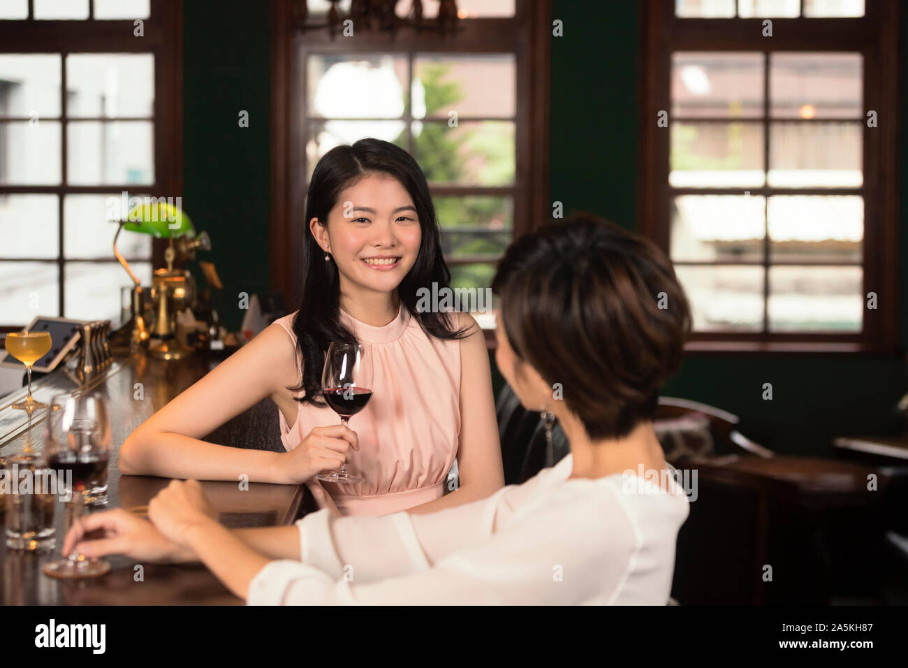 Two smiling young women drinking red wine and talking at bar Stock Photo
