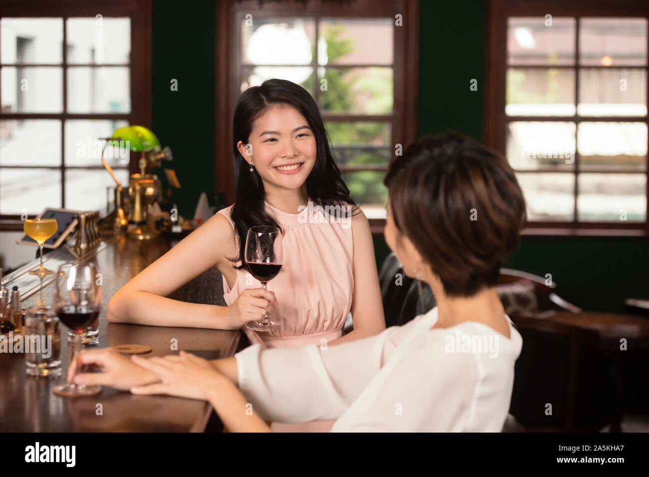 Two smiling young women drinking red wine and talking at bar Stock Photo