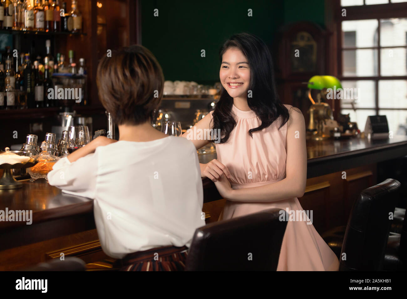 Two smiling young women sitting talking at bar counter Stock Photo