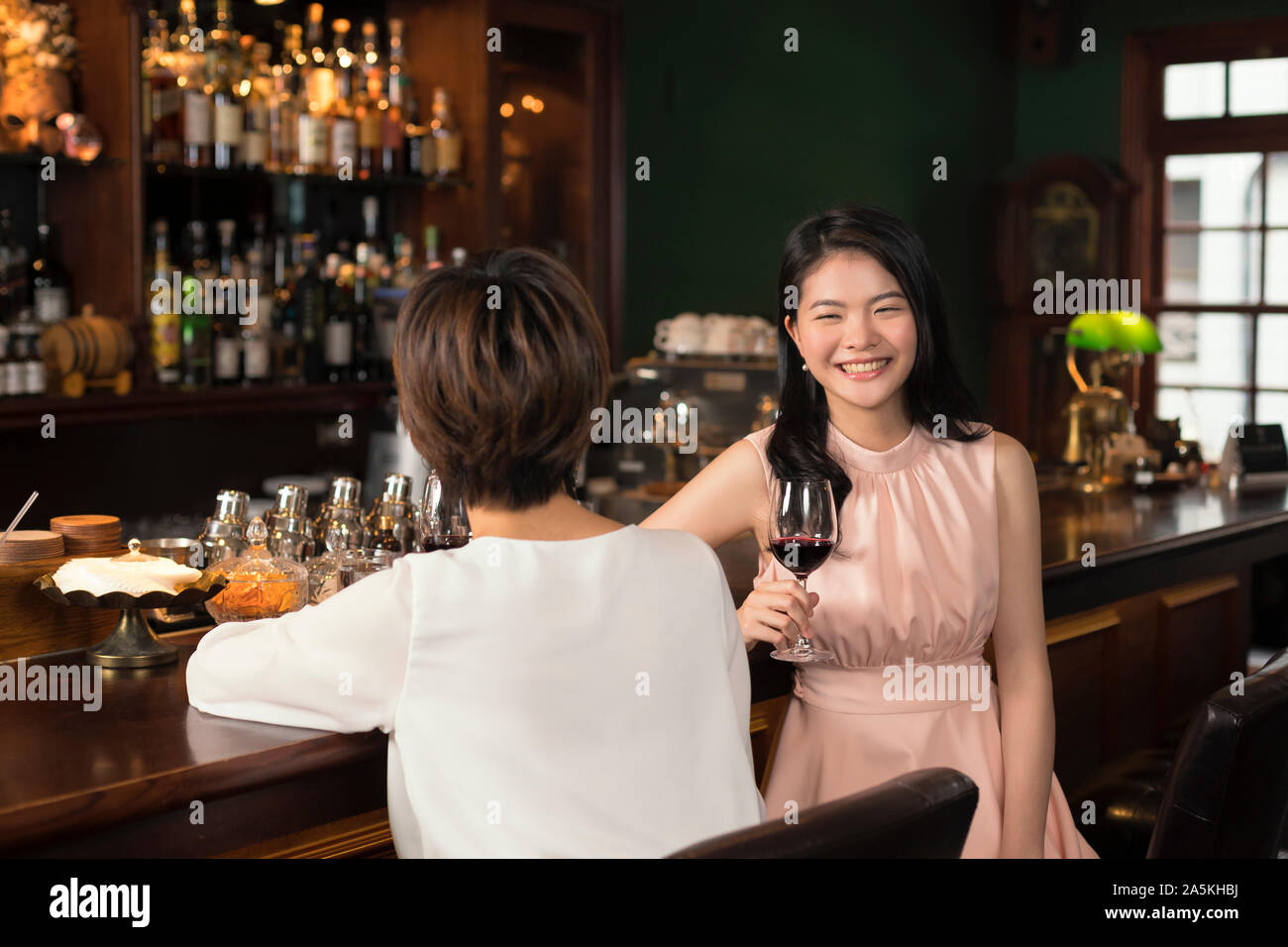 Two smiling young women drinking red wine and talking at bar Stock Photo