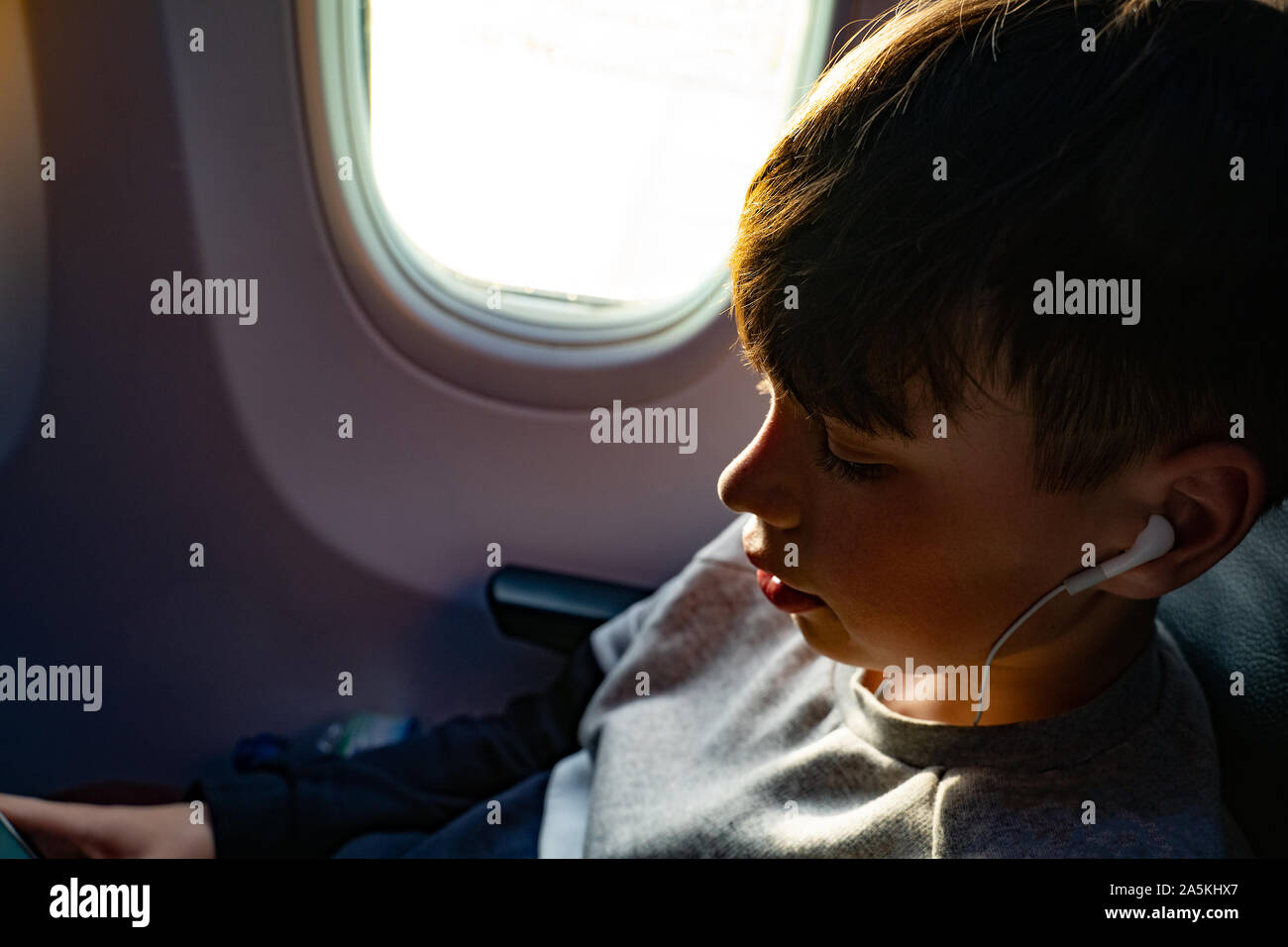 Teenage boy listening to music on earphones during airplane journey, close up Stock Photo