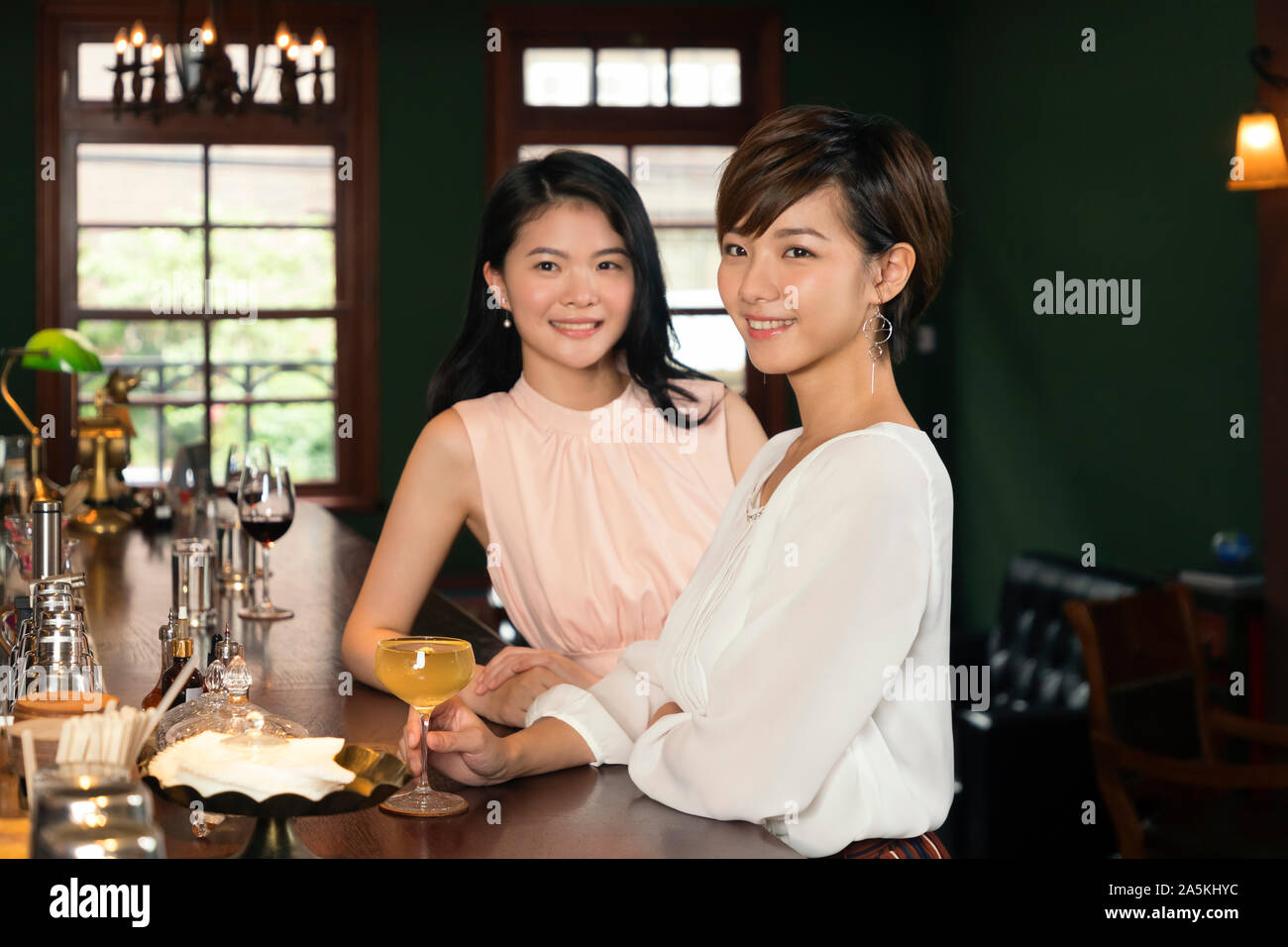 Two smiling young women with cocktail at bar counter Stock Photo