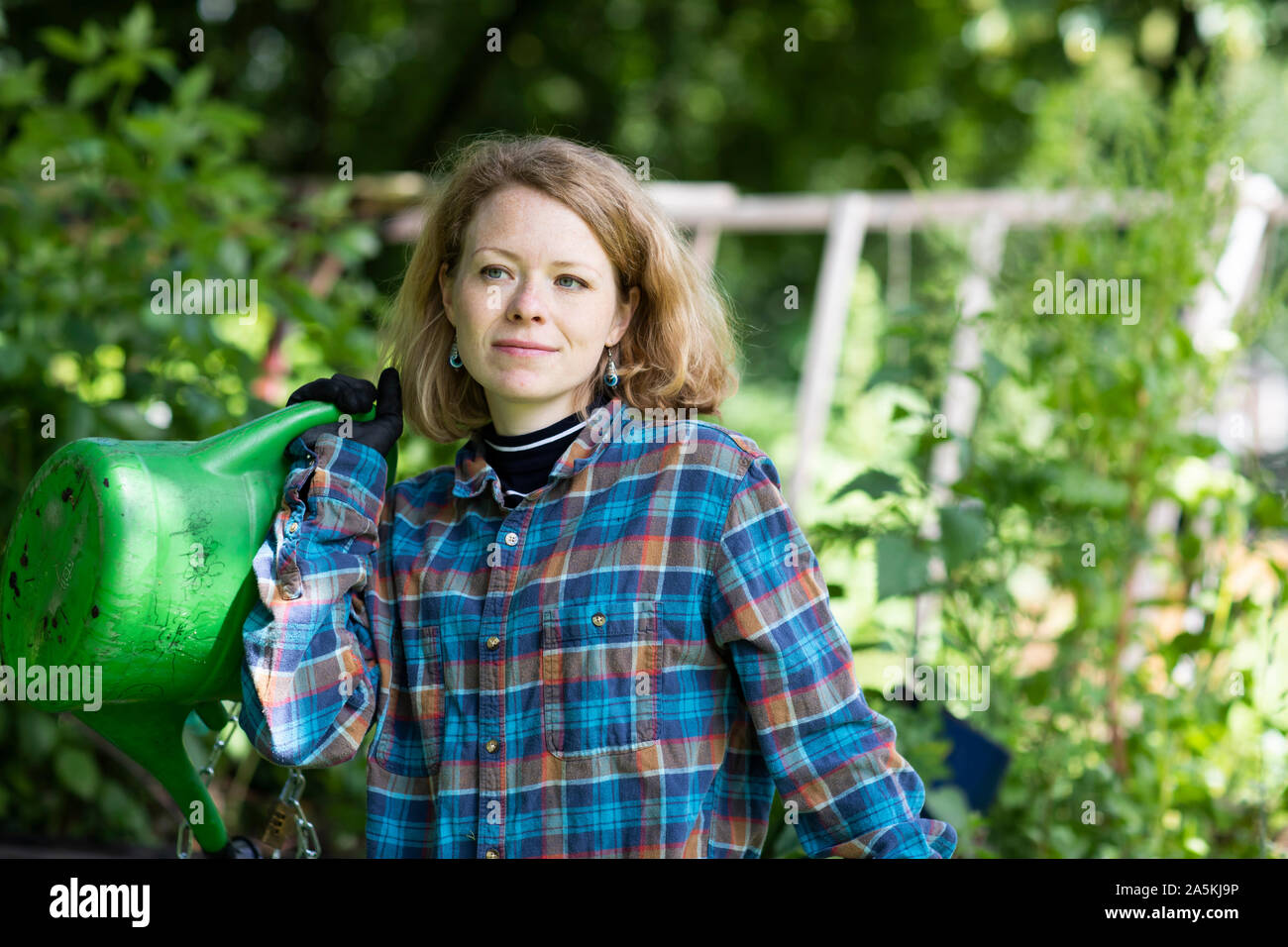 Mid adult woman carrying watering can in her garden Stock Photo