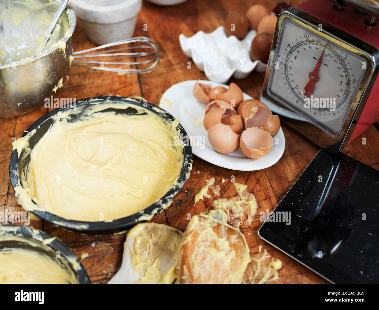 Messy baking preparation on kitchen table with cake mixture, kitchen scales, kitchen utensils and digital tablet Stock Photo