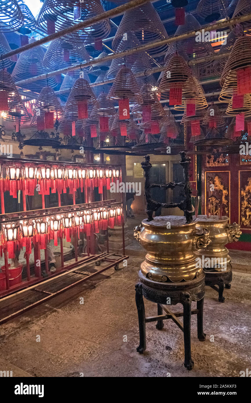 Worshippers inside the Man Mo Temple with giant hanging incense coils is a tribute to the God of Literature and the God of War and was built in 1847 in Sheung Wan District of Hong Kong Island. The Taoist temple is the largest Man Mo Temple in Hong Kong and includes two additional temples for Buddhist and Taoist deities. Stock Photo
