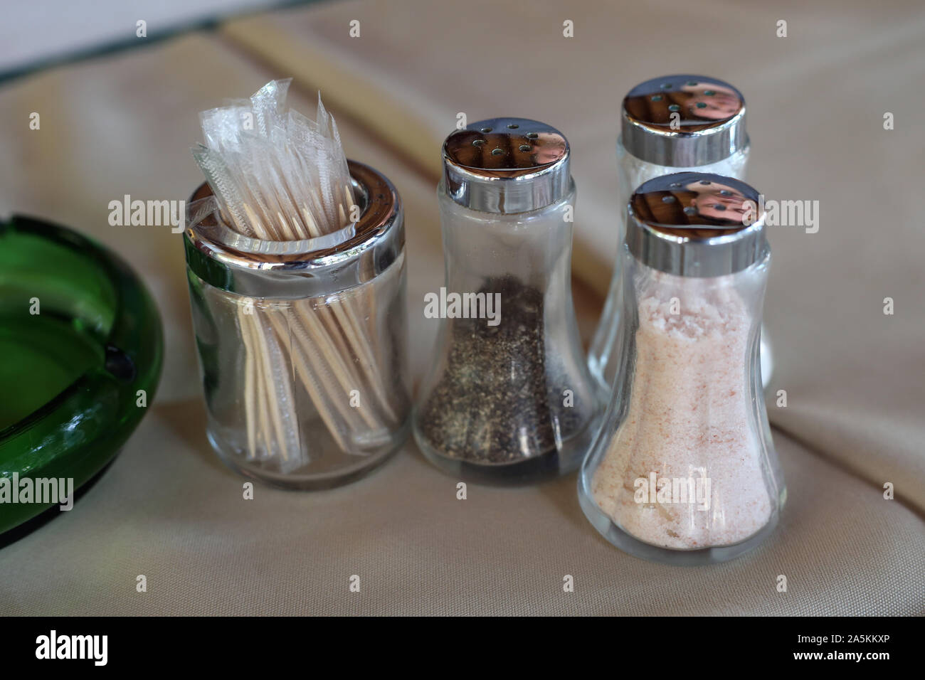 Sugar, salt and pepper shakers made of glass and some toothpicks on a table with beige table cloth. Closeup color image of kitchen details. Stock Photo