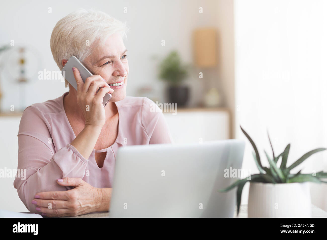 Positive old woman talking by phone with clients Stock Photo - Alamy