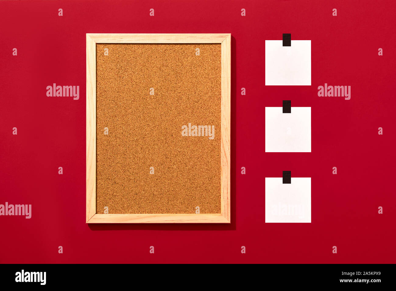 Empty cork board with wooden frame and three blank notes sticked with black tape on red background, top view with copyspace. Stock Photo