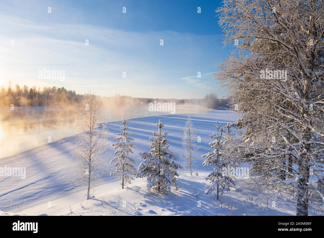 Mist over freezing river on a sunny cold winter day. Trees covered with frost and snow. Stock Photo