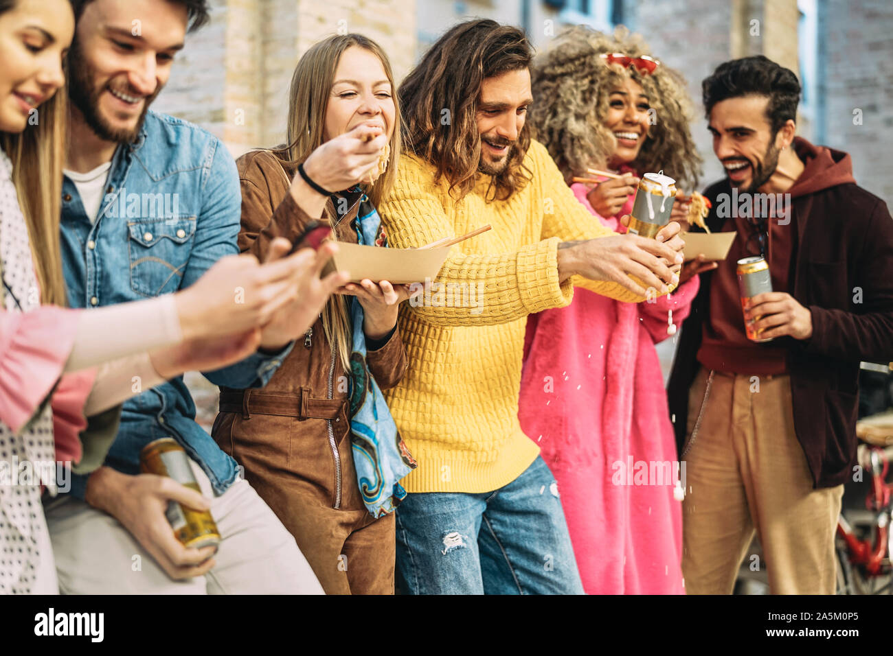 Group of happy friends eating Asian food and drinking beers in the city - Millennial young people having fun and laughing together outdoor Stock Photo