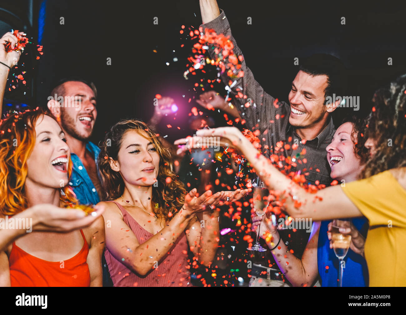 Happy friends doing party throwing confetti in the club - Millennial young people having fun celebrating in the nightclub Stock Photo