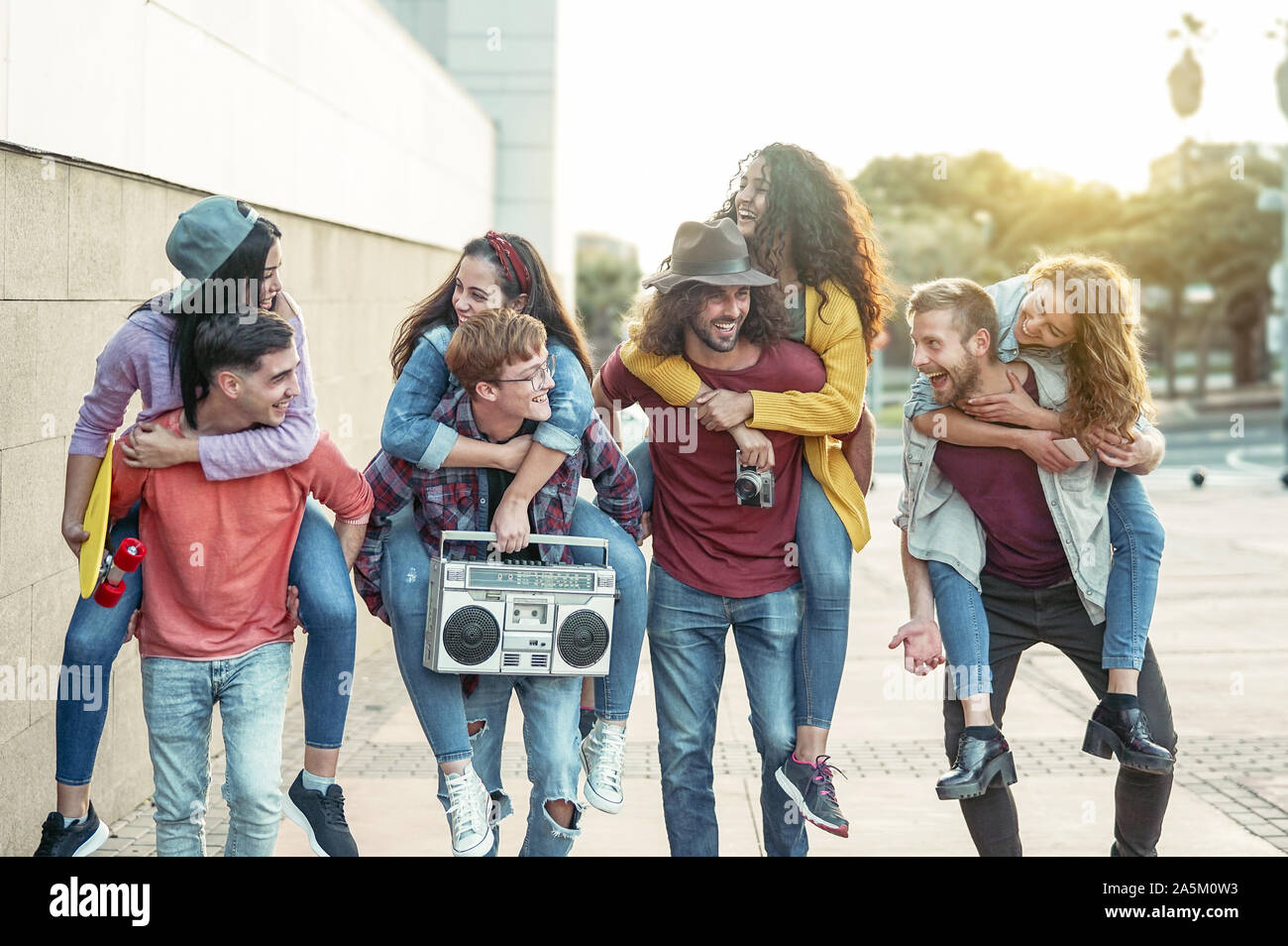 Happy millennials friends having fun outdoor - Young people piggybacking while laughing and walking together in the city center Stock Photo