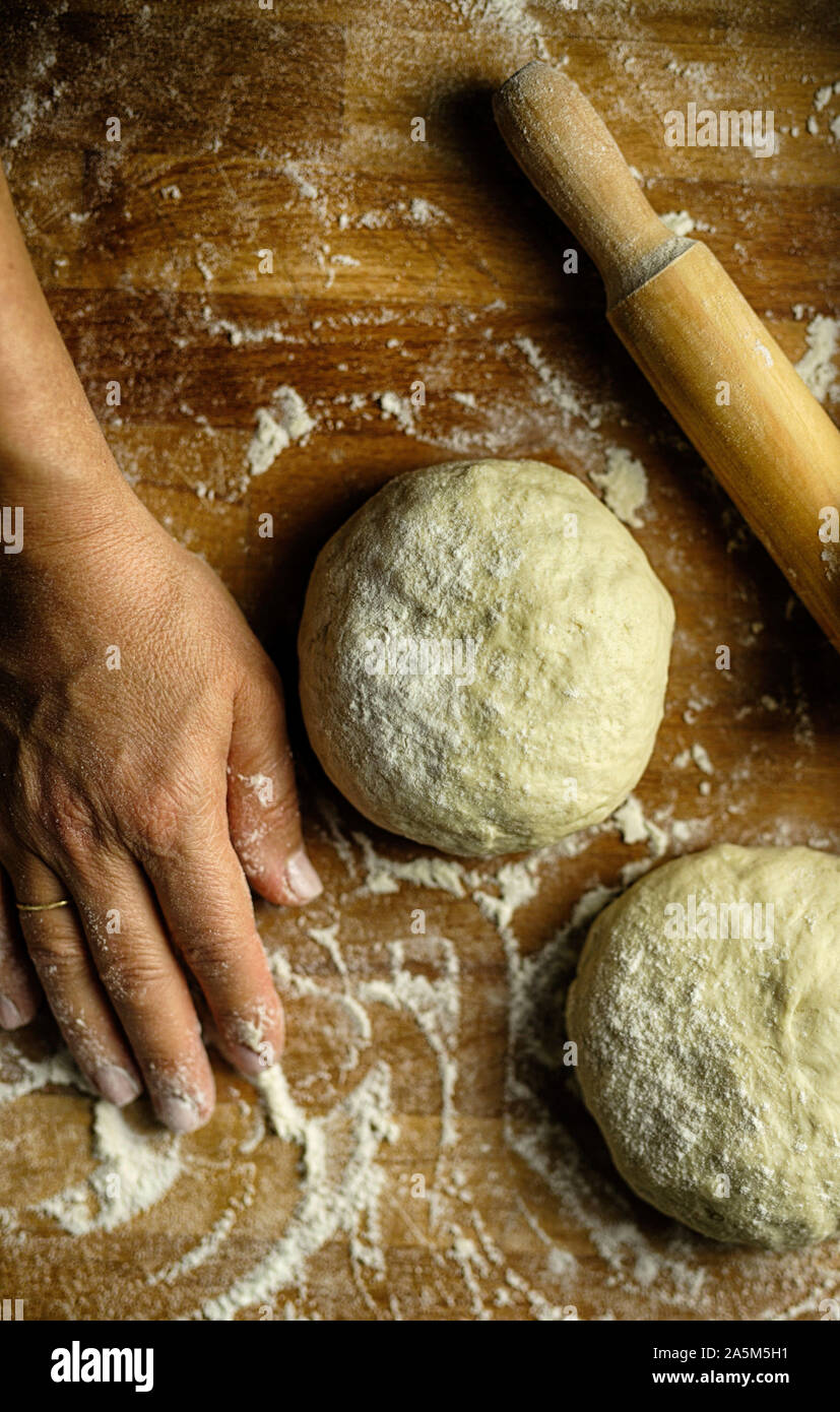 Preparing traditional homemade pasta. Fresh dough, rolling pin and woman's hand resting after kneading dough on floured wooden table. Top view Stock Photo