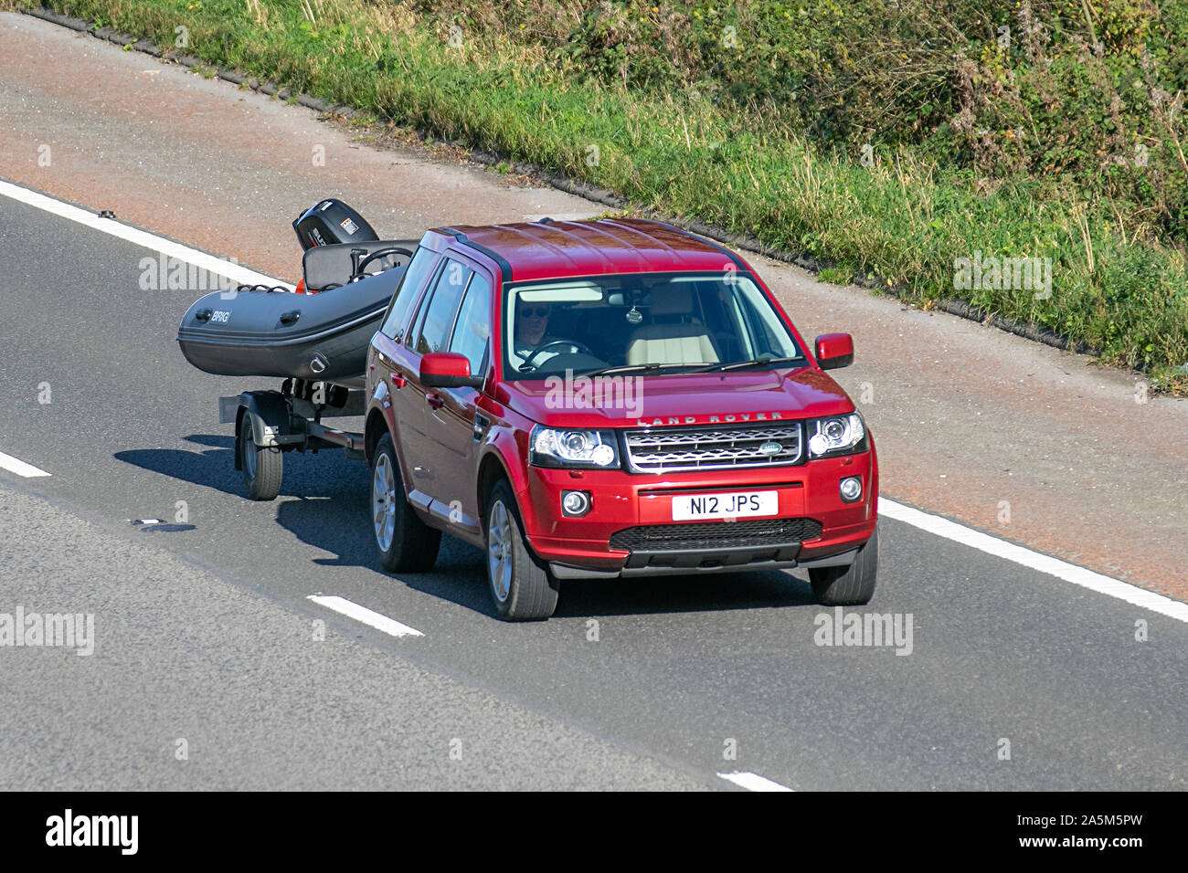 2014 red Land Rover Freelander SE SD4 Auto towing boat trailer; UK Vehicular traffic, transport, modern, saloon cars, south-bound on the 3 lane M6 motorway highway. Stock Photo