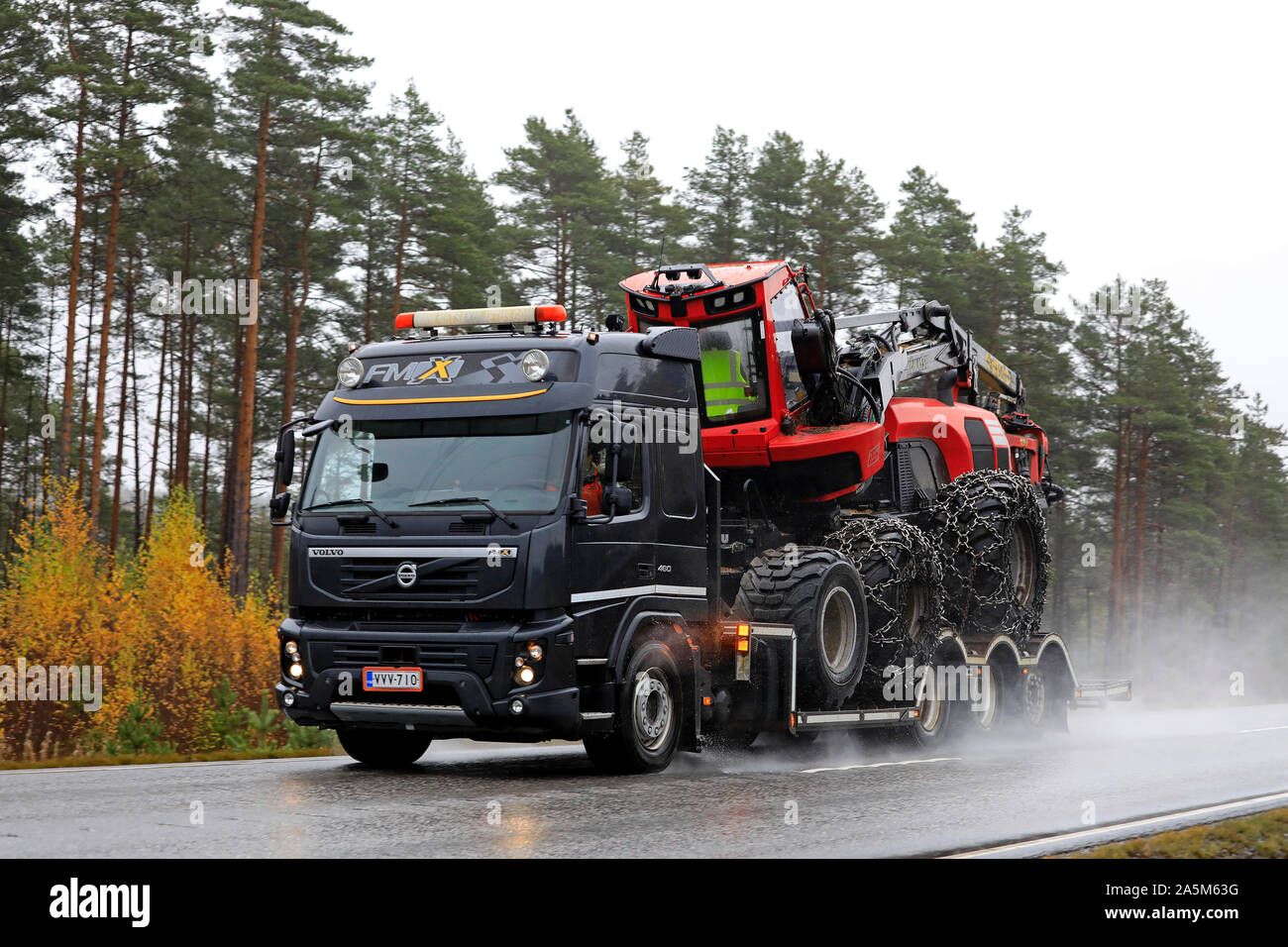 Black Volvo FMX of Metsakuljetus transports Komatsu 911 forest harvester on trailer on wet highway in autumn. Tenhola, Finland. October 18, 2019. Stock Photo