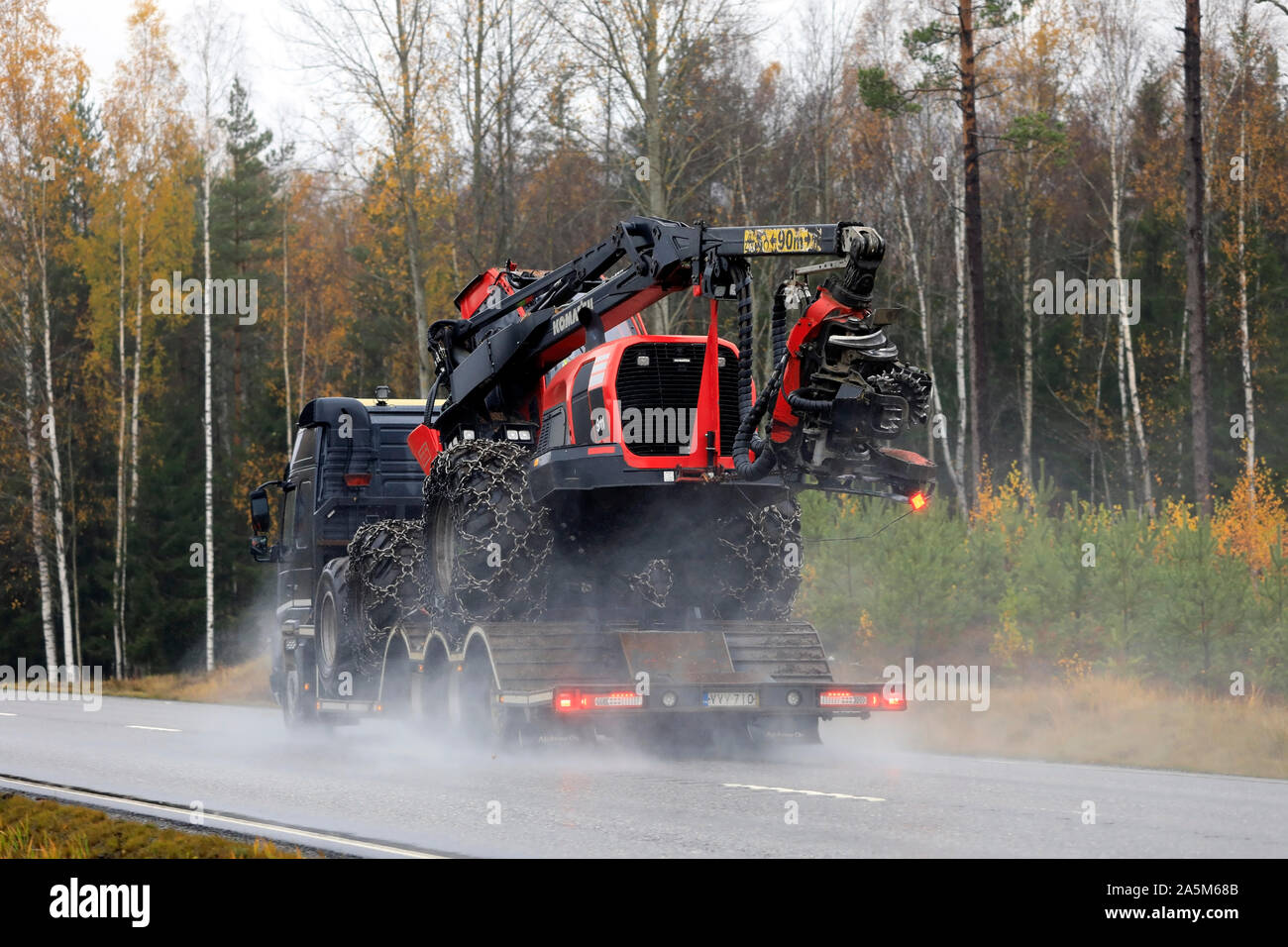 Black Volvo FMX truck hauls Komatsu 911 forest harvester on trailer on wet highway in autumn. Rear view. Tenhola, Finland. October 18, 2019. Stock Photo