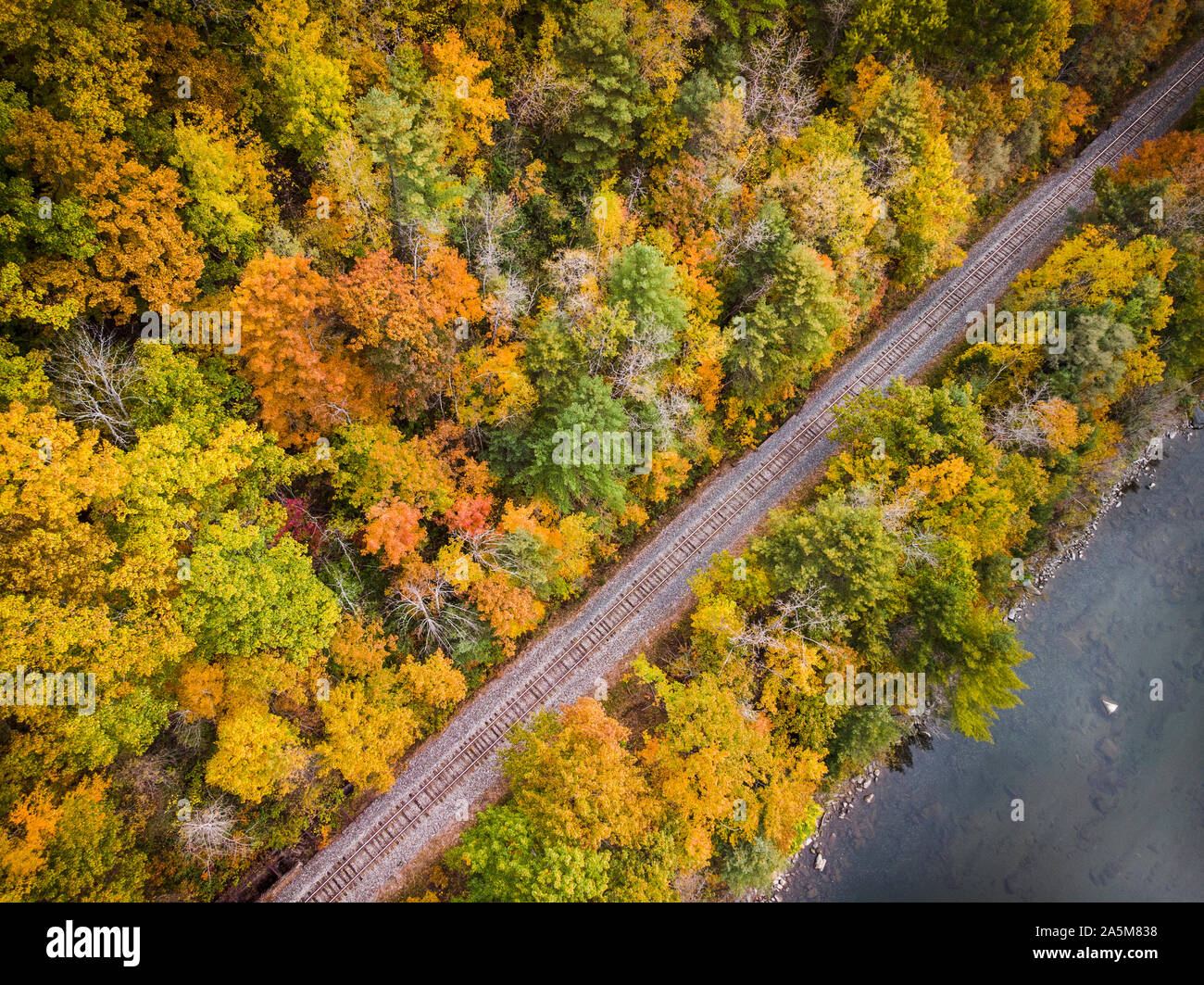 Fall foliage lines a train track alongside Vermont's White River. Stock Photo