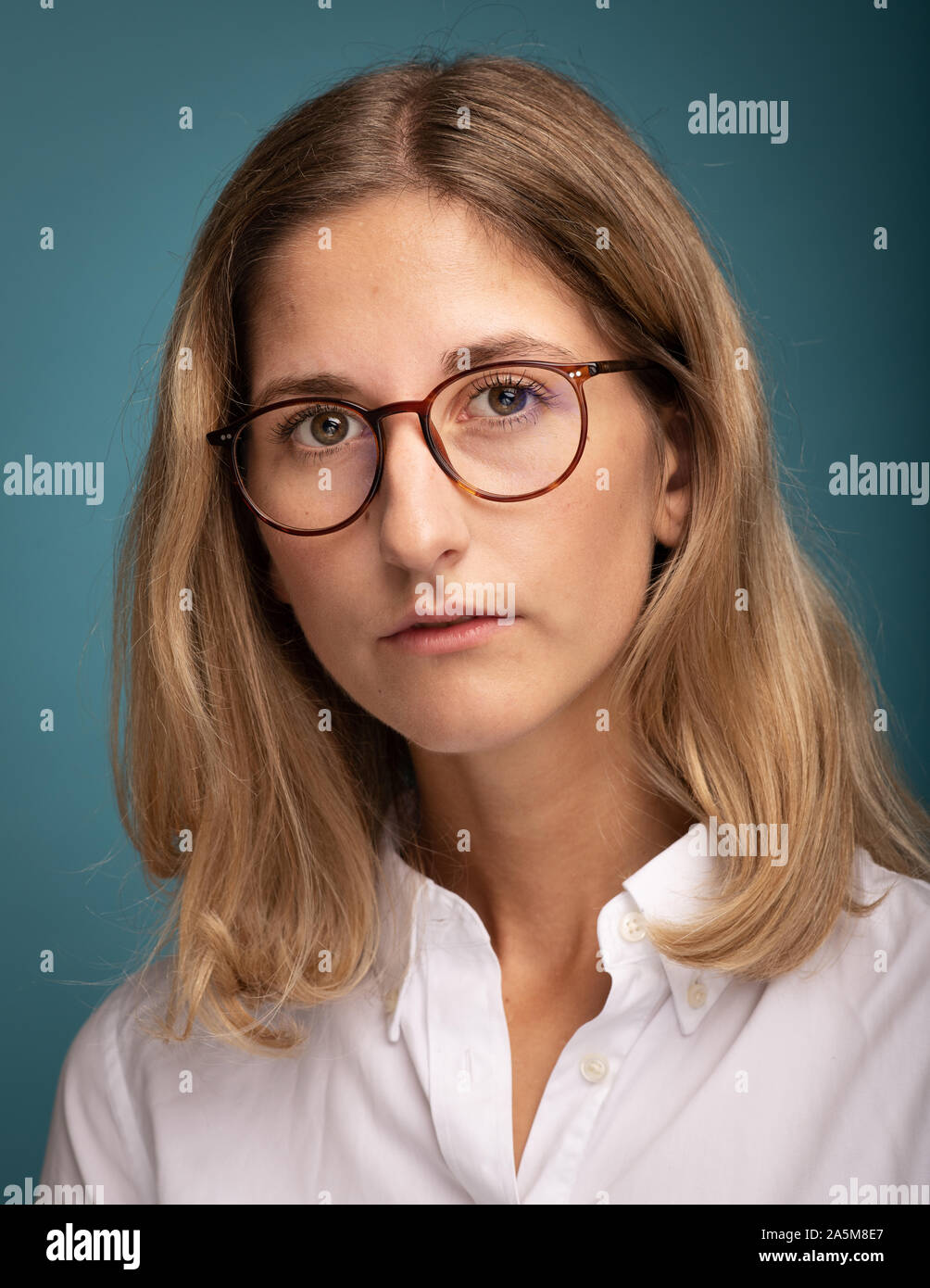Portrait of a blonde businesswoman wearing glasses in front of blue background Stock Photo