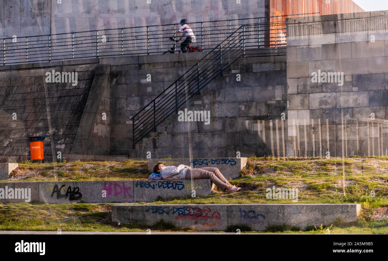 Boy resting on stone bench, friend cycling in background, Berlin, Germany Stock Photo