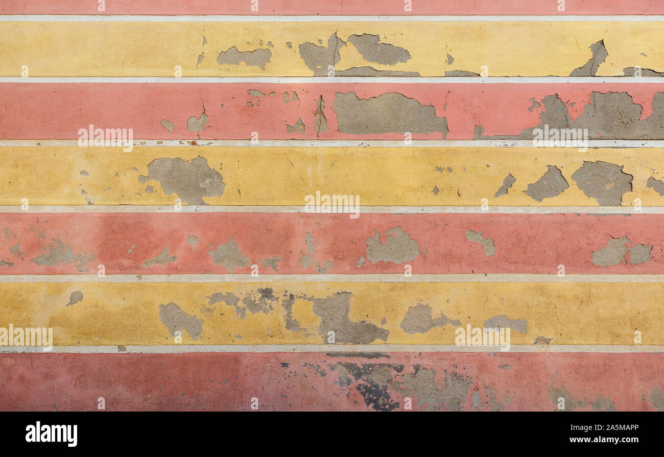 Weathered and old concrete wall with horizontal yellow and red stripes, paint is peeling off. High resolution abstract full frame textured background. Stock Photo