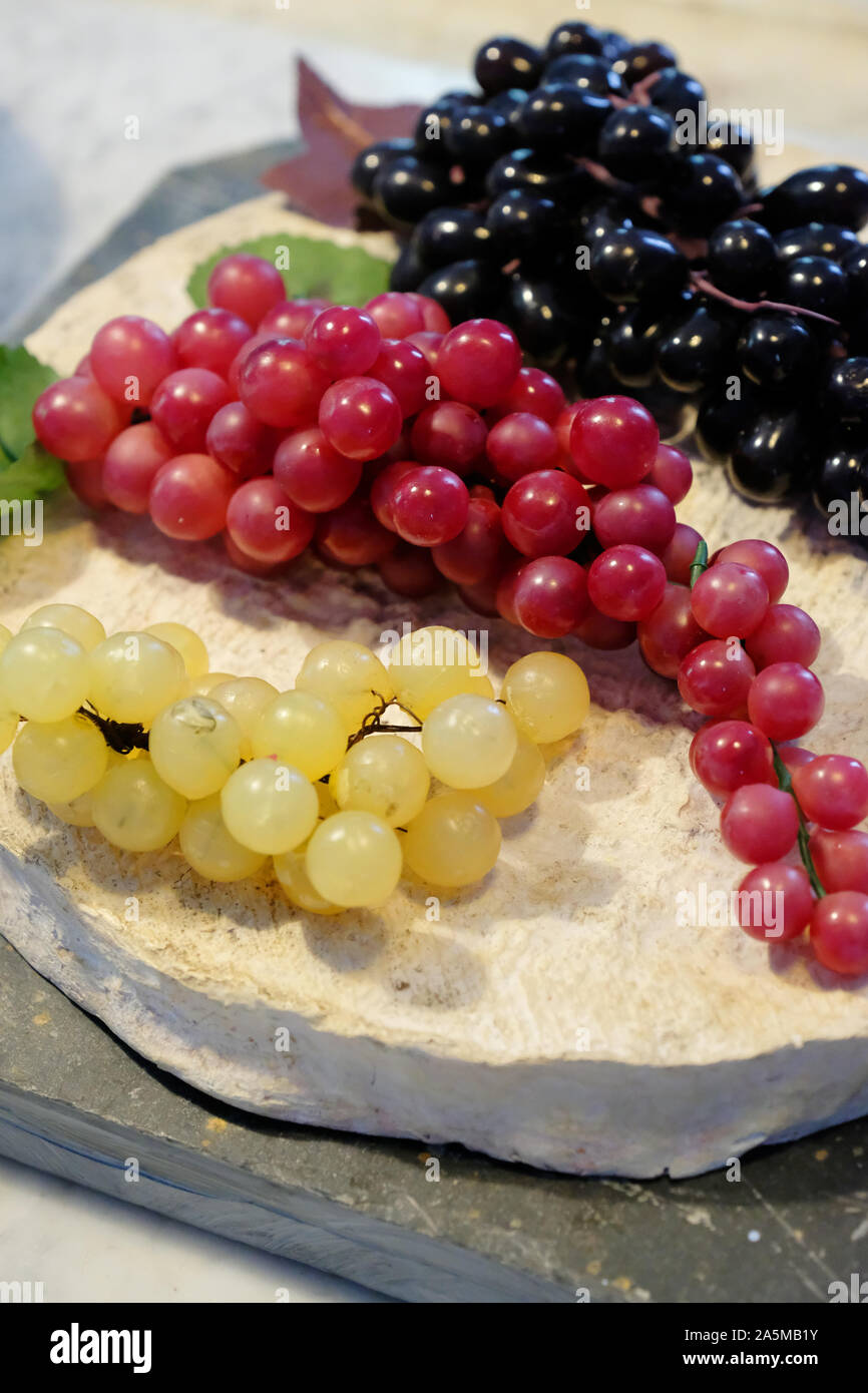 A selection of bunches of grapes resting on a large cheese - John Gollop Stock Photo