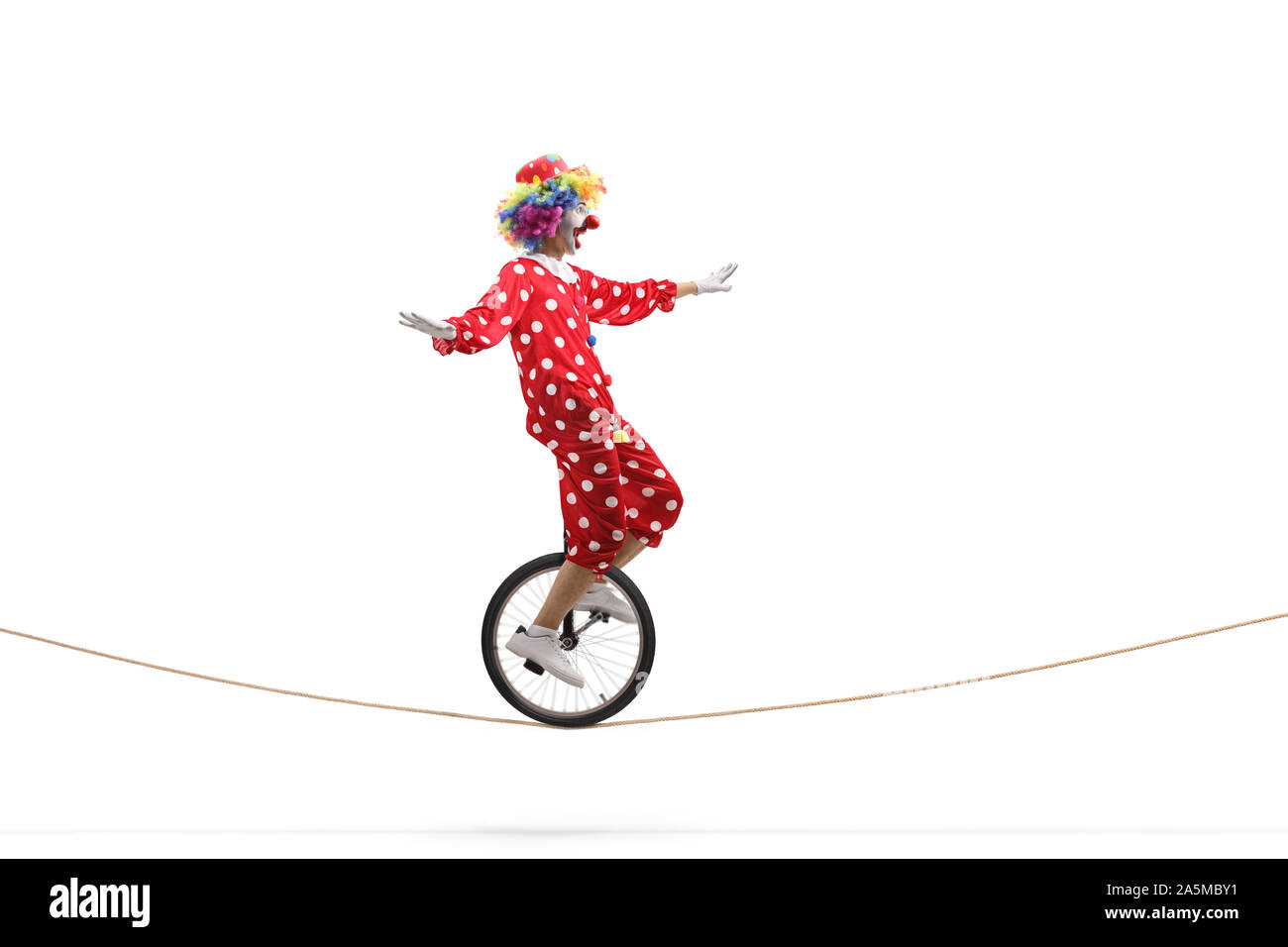Full length profile shot of a scared clown riding a unicycle on a rope isolated on white background Stock Photo