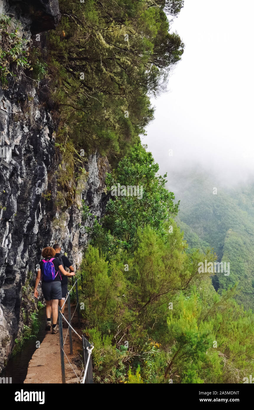 Tourists walking on a narrow path on the edge of the rock during Levada ...