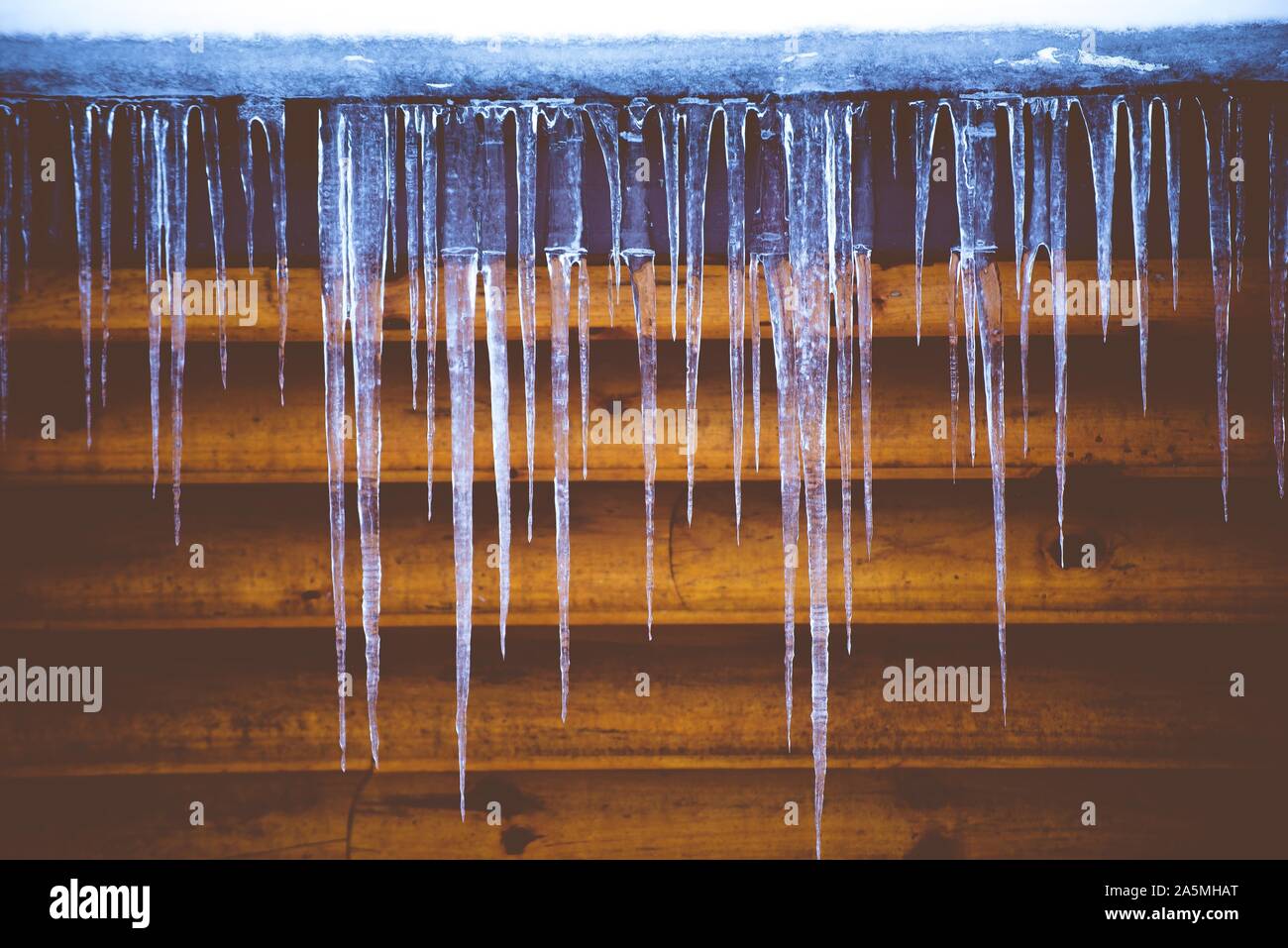 Closeup shot of ice cycles with a wooden wall in the background Stock Photo