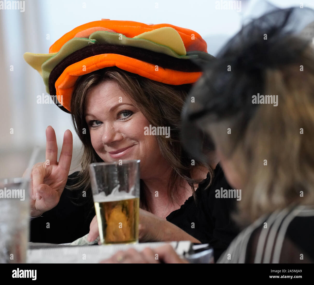 A woman in a very colorful hat enjoys a beer at the bar during Ladies Day at Arizona Downs, Prescott Valley, Arizona on August 10, 2019. Stock Photo