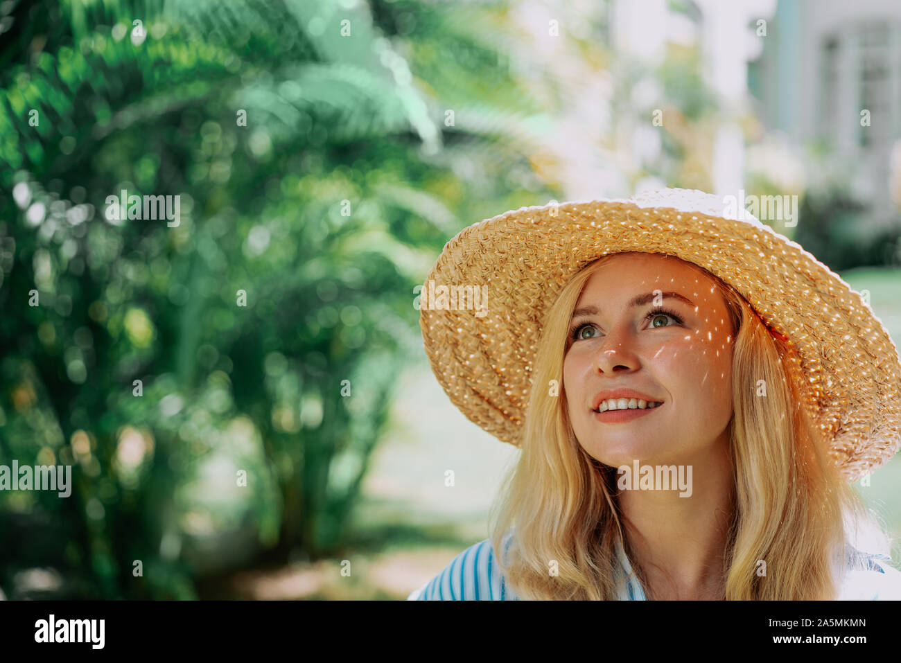 Portrait of beautiful of traveler woman with hat smiling behind palm trees. Sunlight. Concept travel, vacation, dream Stock Photo