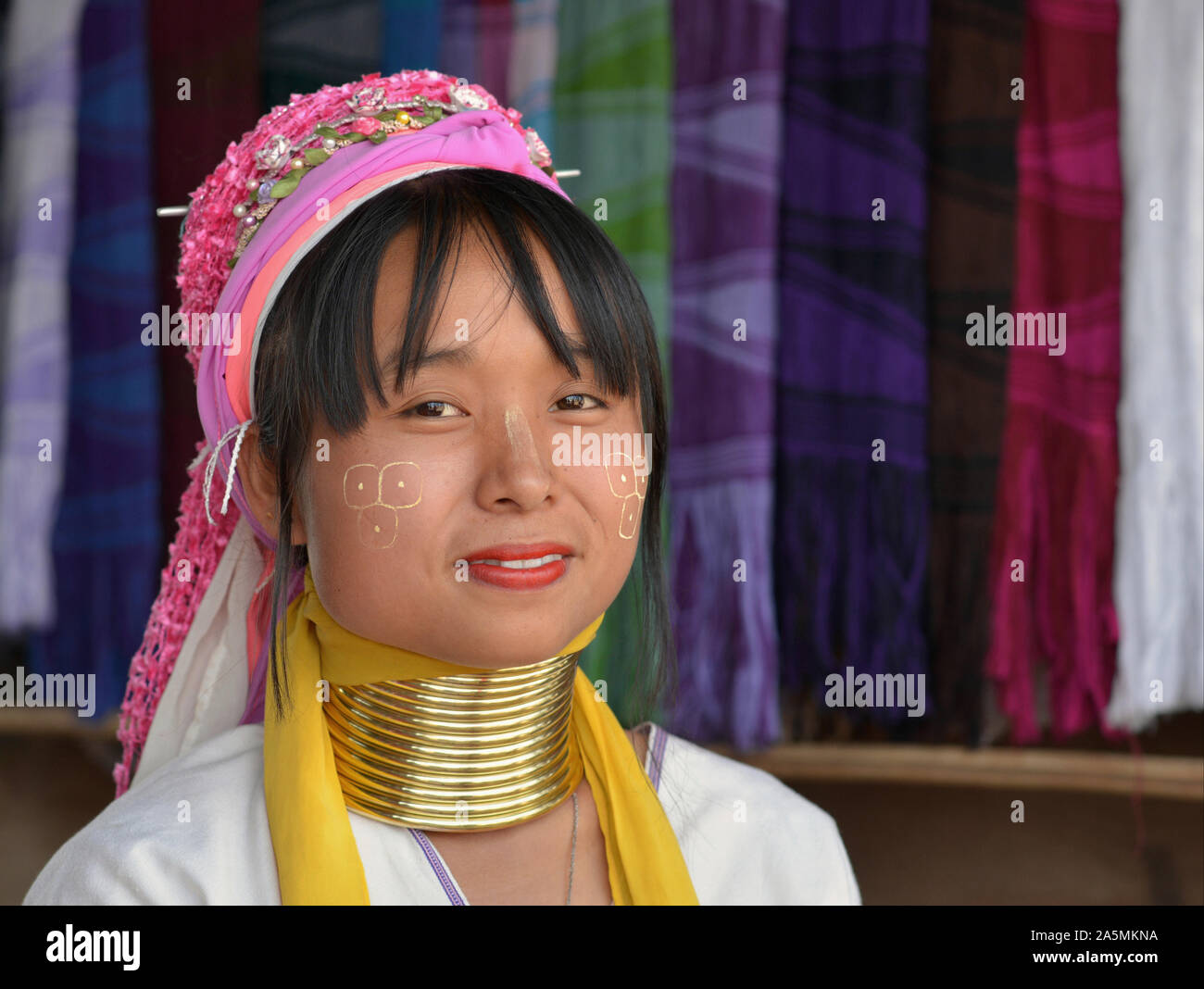 Young Myanmarese Kayan Lahwi longneck woman (“giraffe woman”) with thanaka face cosmetic and tribal Padaung brass neck rings smiles for the camera. Stock Photo