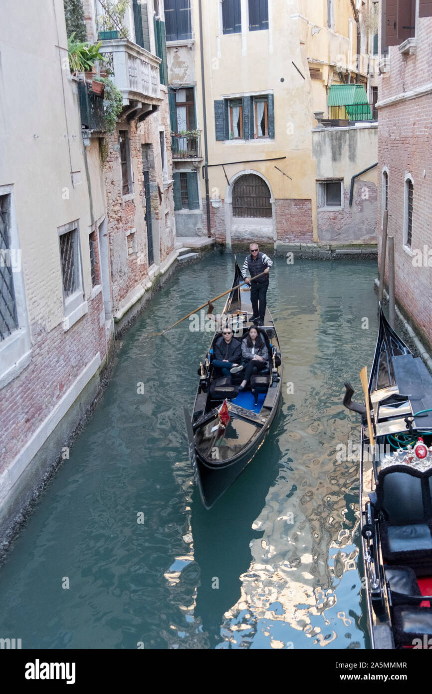 An Asian couple, likely Chinese, take a gondola ride on a  side street   Canal in Venice, Italy. Stock Photo