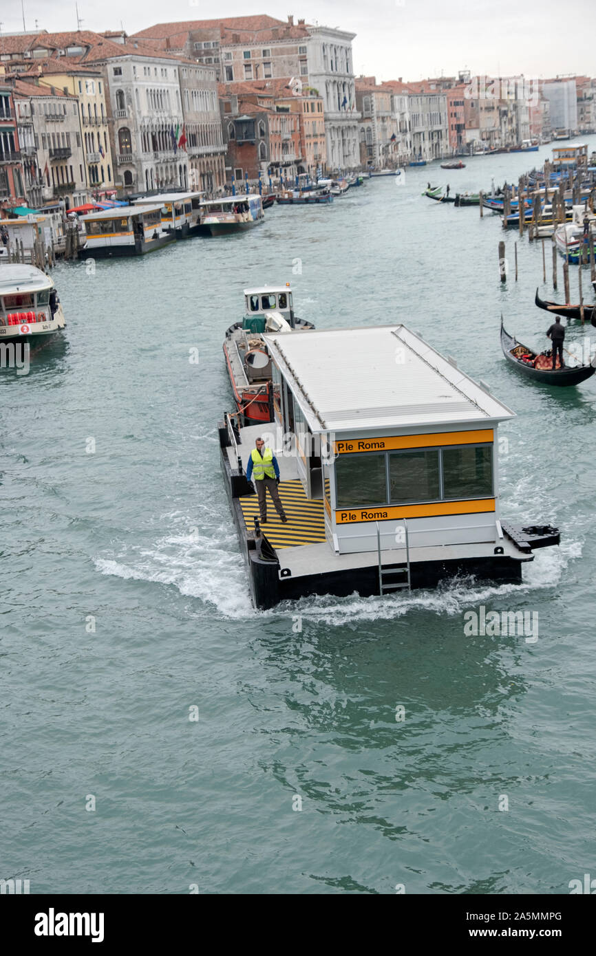 The Piazzale Roma vaporetto station is pushed by a tug boat, likely for repair or refurbishing. From the Rialto Bridge on  the Grand Canal in Venice. Stock Photo