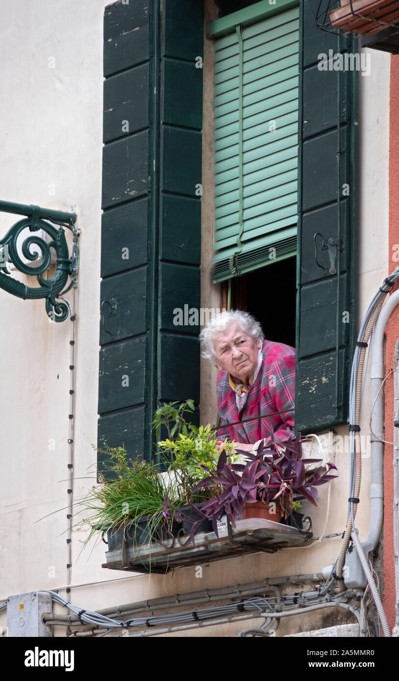 An older Venetian women deep in thought as she gazes out of her window at Campo Marina in Venice, Italy. Stock Photo