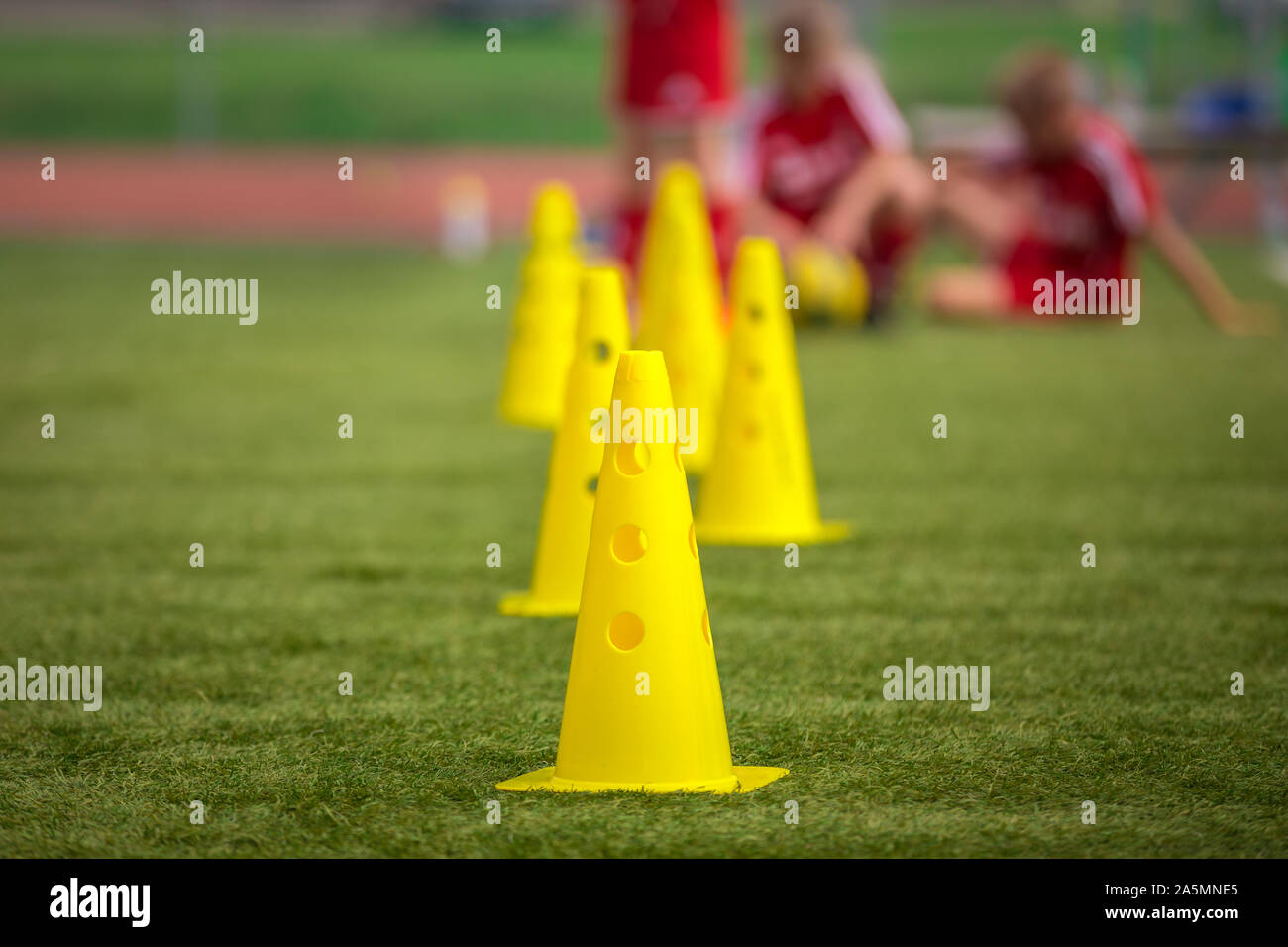 Yellow soccer training cones on grass field. Youth football players on training in the background. School soccer outdoor practice for elementary age k Stock Photo