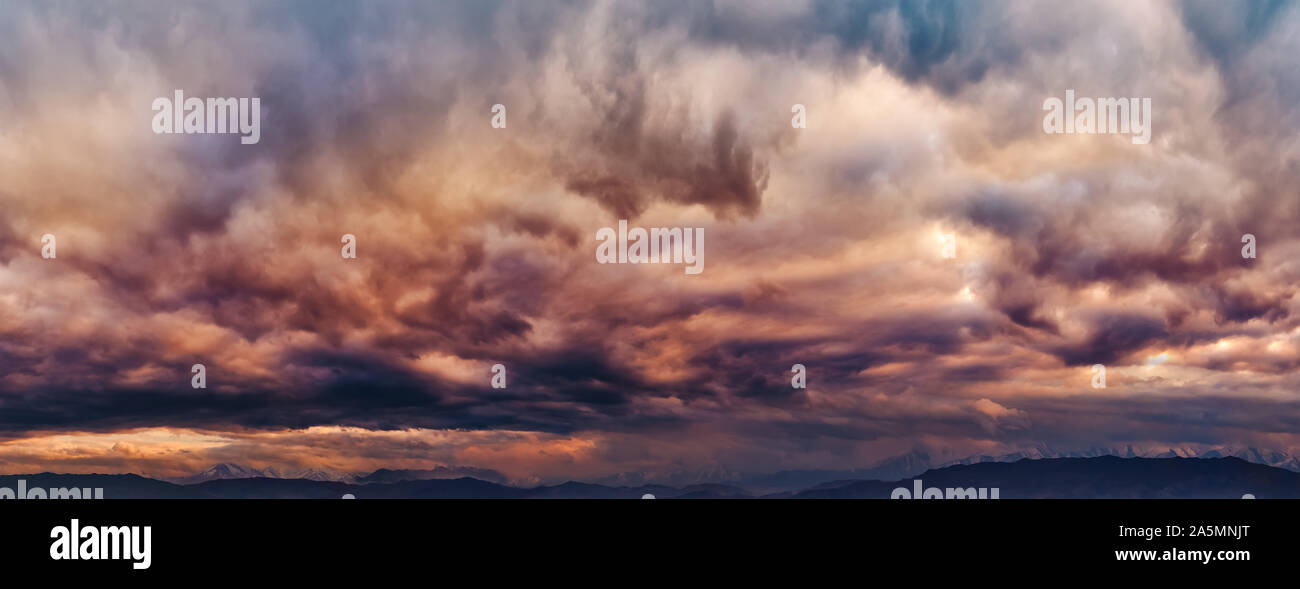 Dramatic light through the clouds against the backdrop of an exciting, vibrant stormy sky at sunset, dawn in the mountains. panorama, natural composit Stock Photo