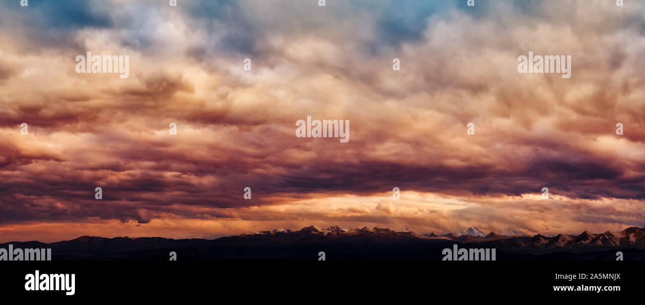 Dramatic light through the clouds against the backdrop of an exciting, vibrant stormy sky at sunset, dawn in the mountains. panorama, natural composit Stock Photo
