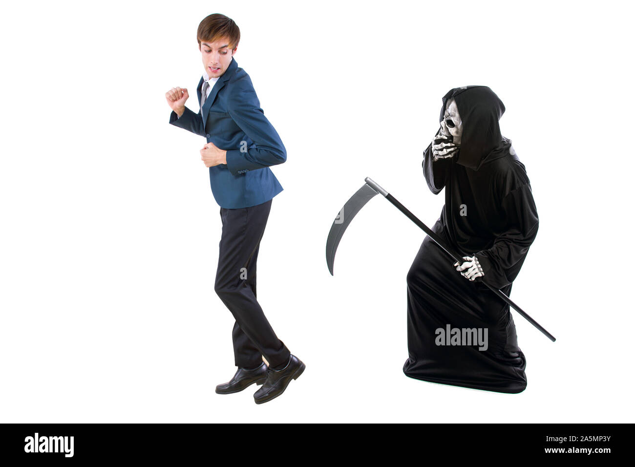 Man in a Halloween grim reaper ghost costume chasing, mocking and making fun of scared businessman running away.  Can also depict death following a ma Stock Photo