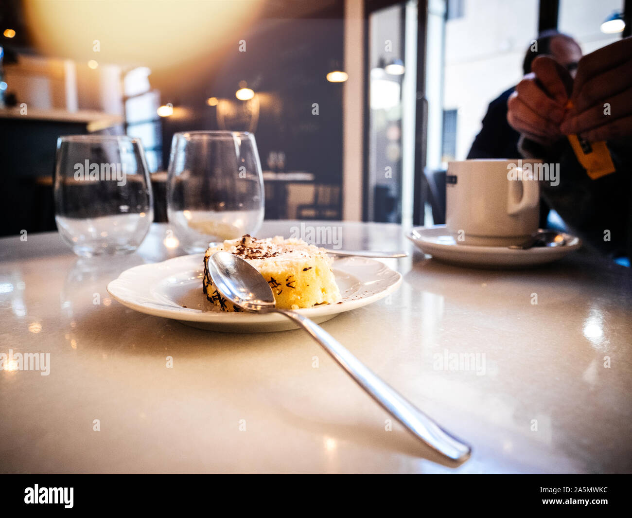 Spoon on the plate with traditional Catalan Spanish cake in cozy cafe interior and woman silhouette open a tea bag Stock Photo