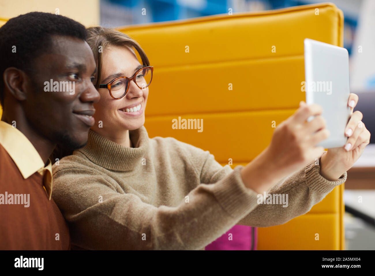 Portrait of two college students taking selfie via digital tablet while relaxing in library lounge, copy space Stock Photo