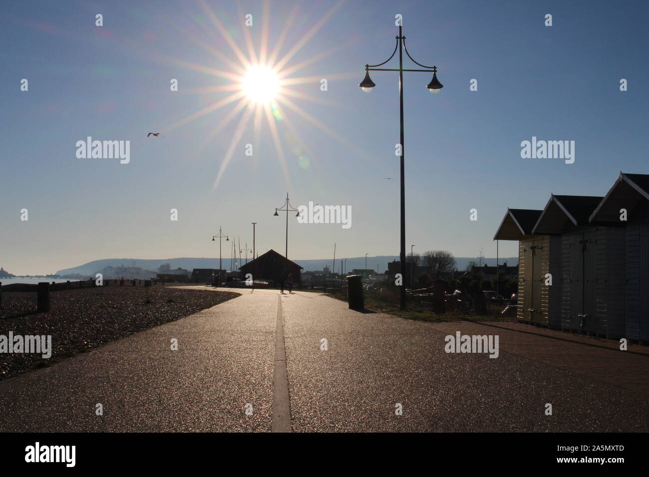Looking into the sun above the eastern promenade that runs alongside the shingle beach of Eastbourne on the south coast of England. Stock Photo