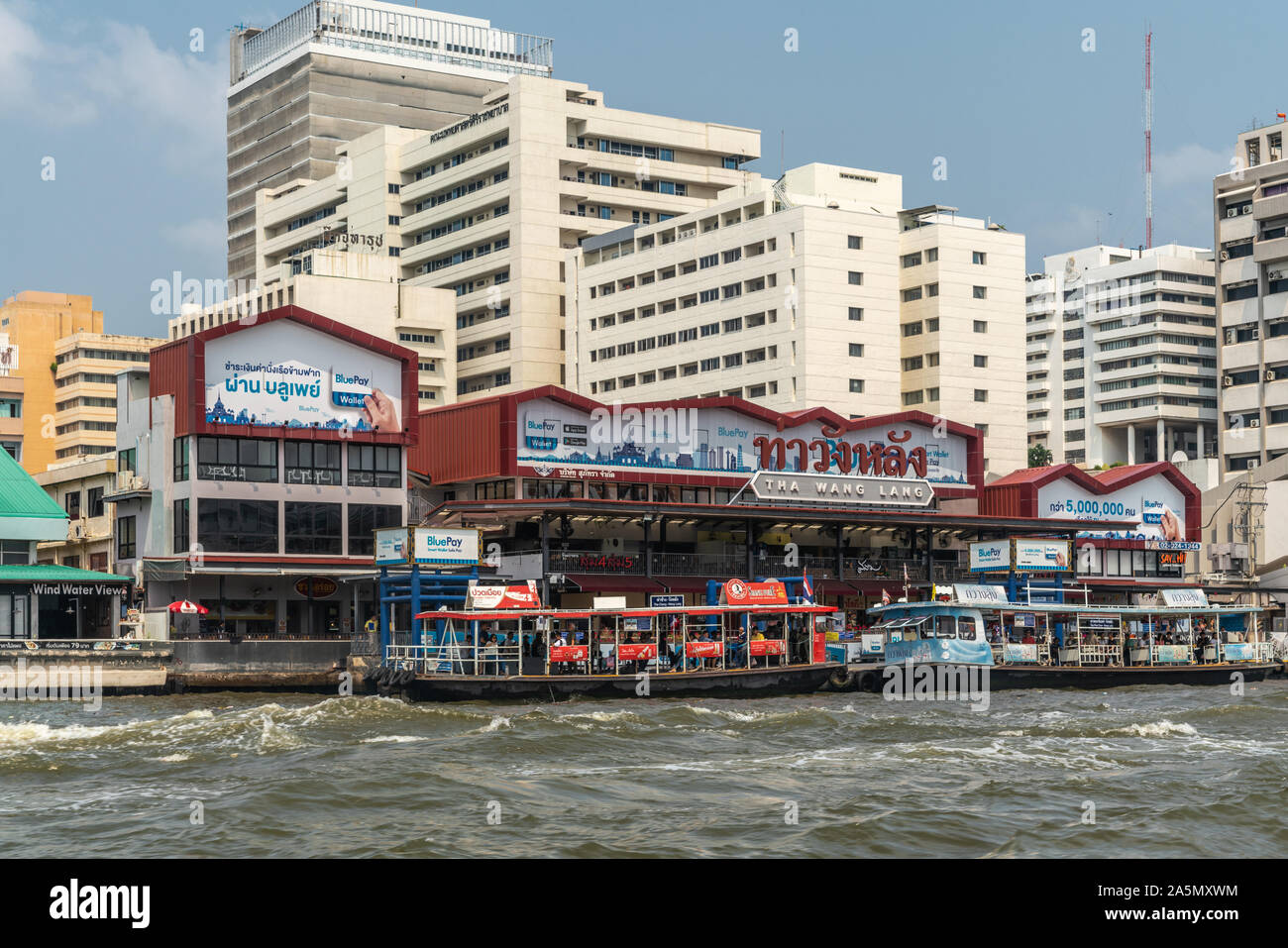 Bangkok city, Thailand - March 17, 2019: Chao Phraya River. Maroon painted Tha Wang Lang market and shopping mall with ferries docked in front. White Stock Photo