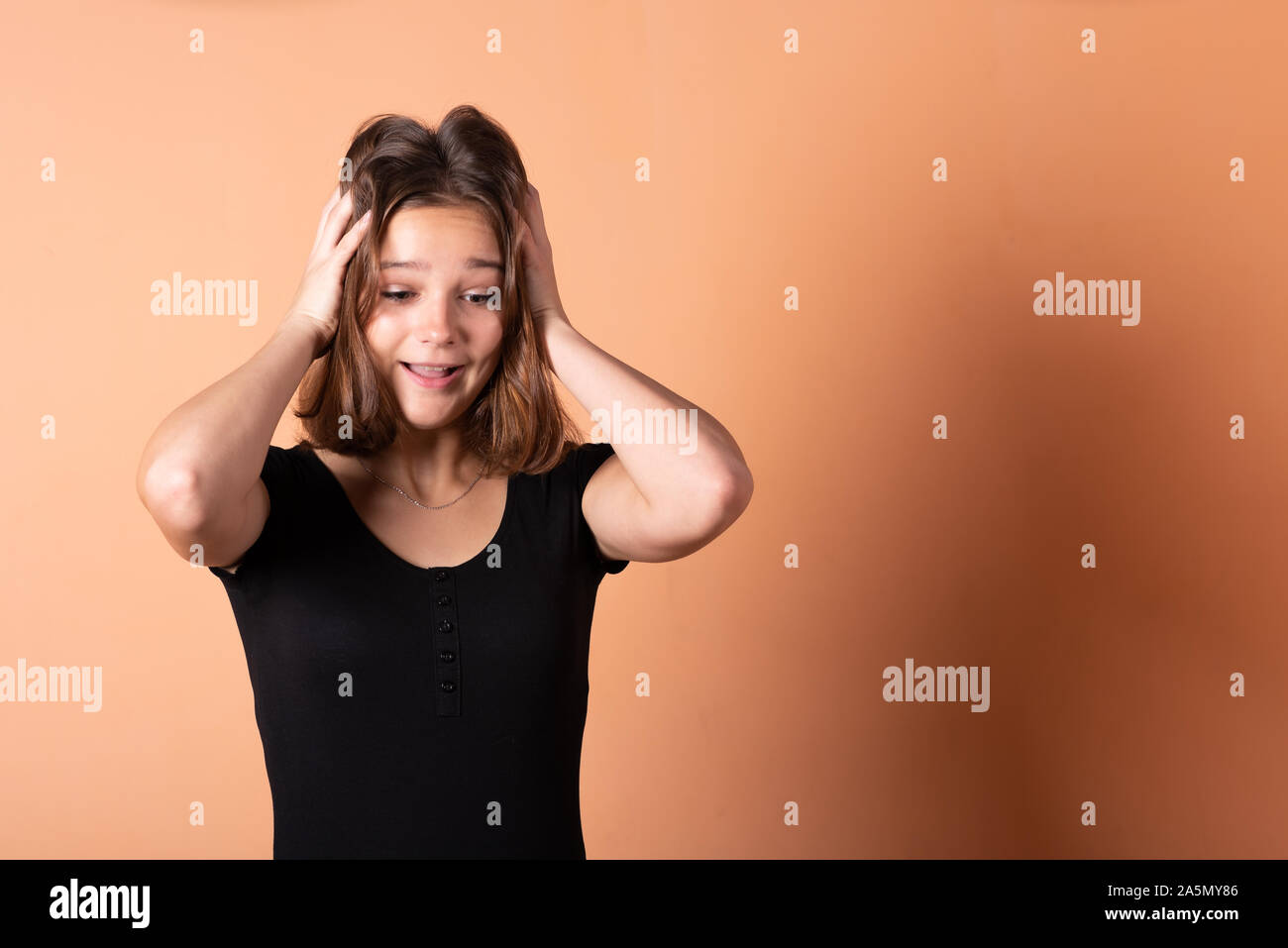 The girl is worried and holds on to her head, on a light orange background. Stock Photo