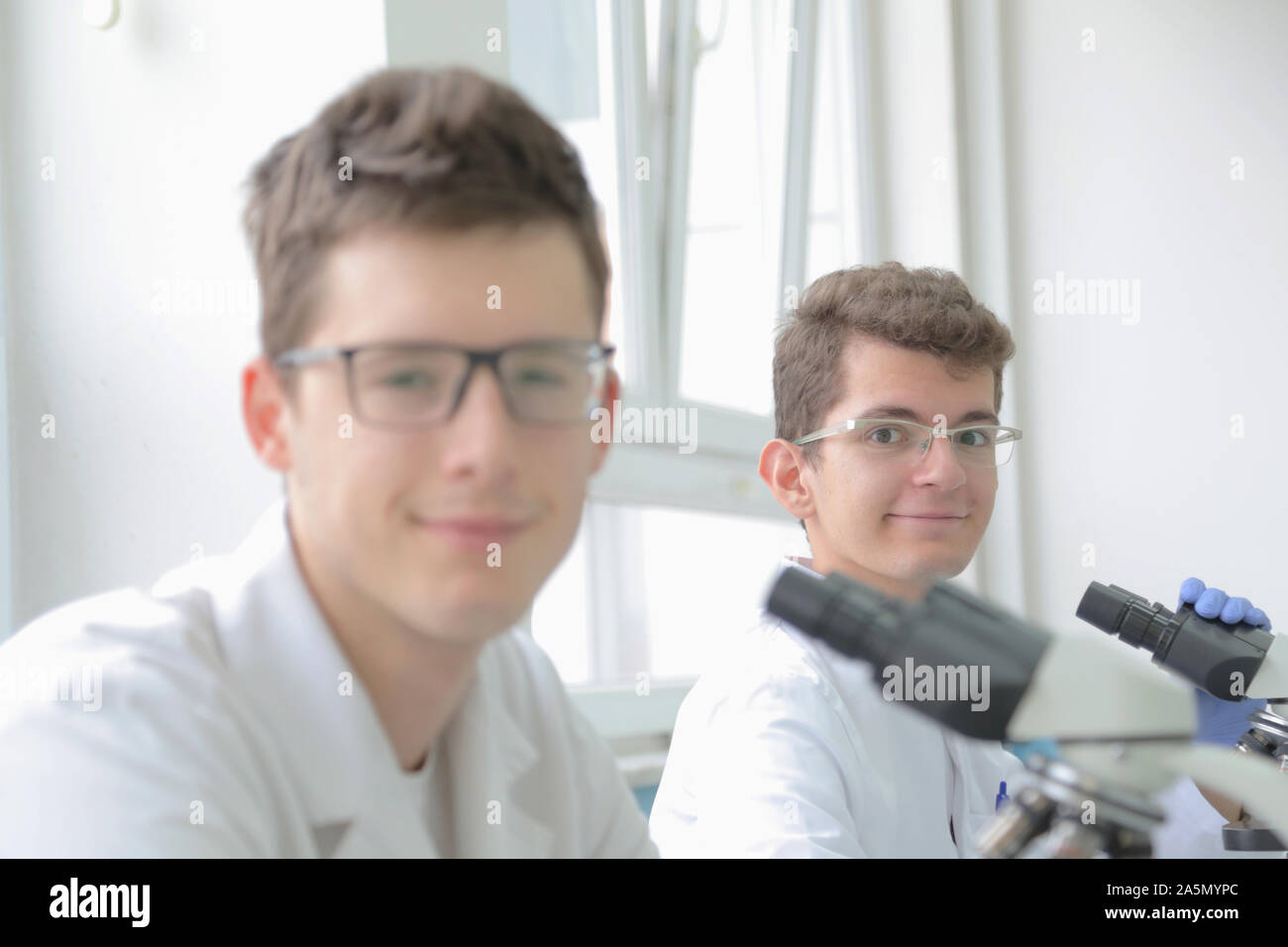 Two Young male scientists looking through a microscope in a laboratory ...